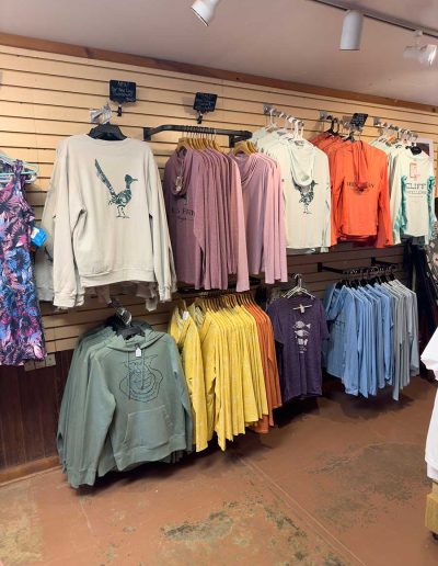 lees ferry gallery 12 Colorful sweatshirts and shirts displayed on wooden racks.